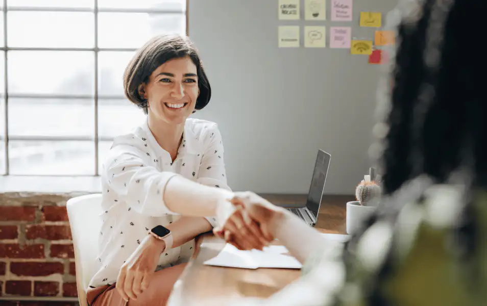 Woman at desk shaking hands and smiling