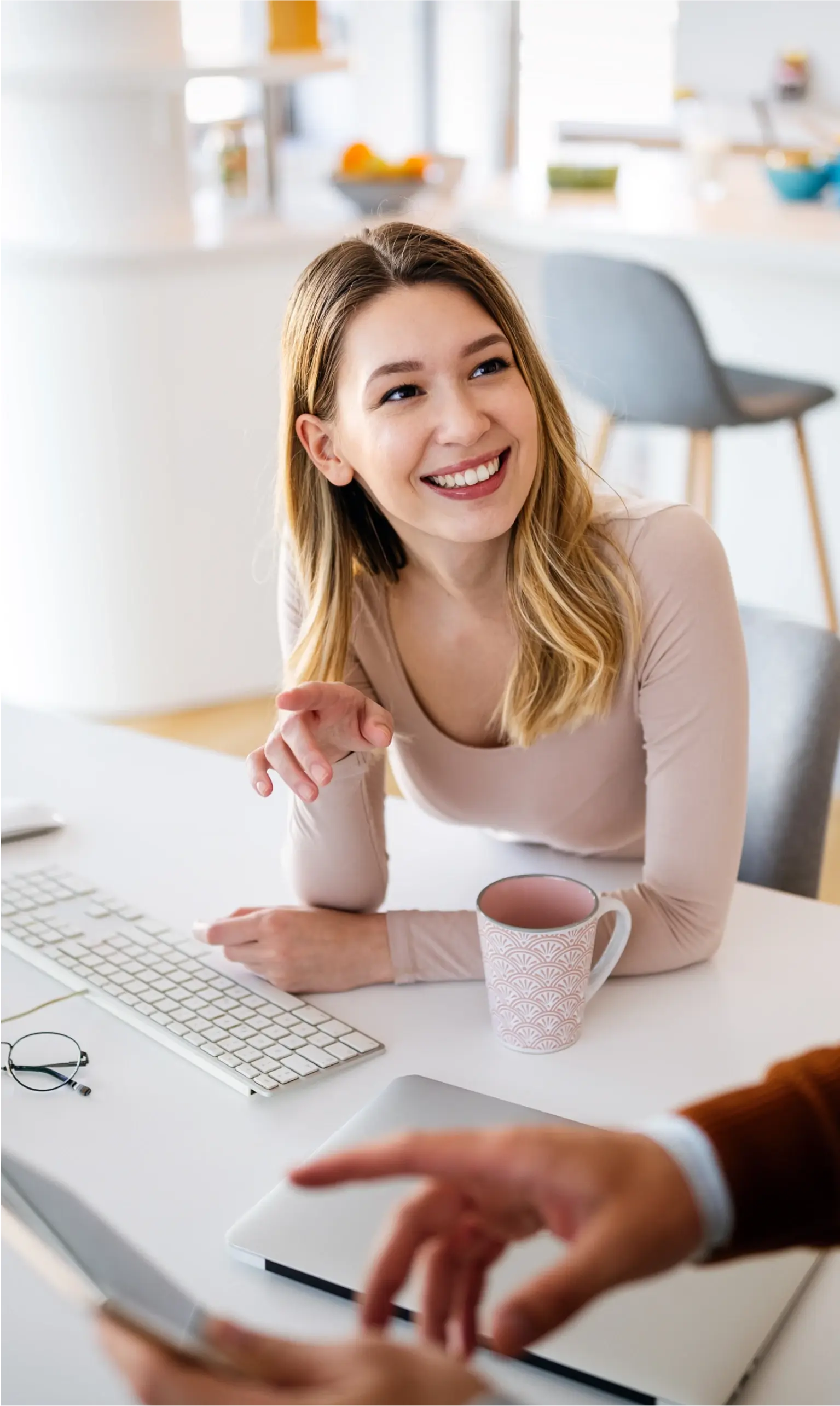 Woman at her desk with coffee smiling talking to another employee