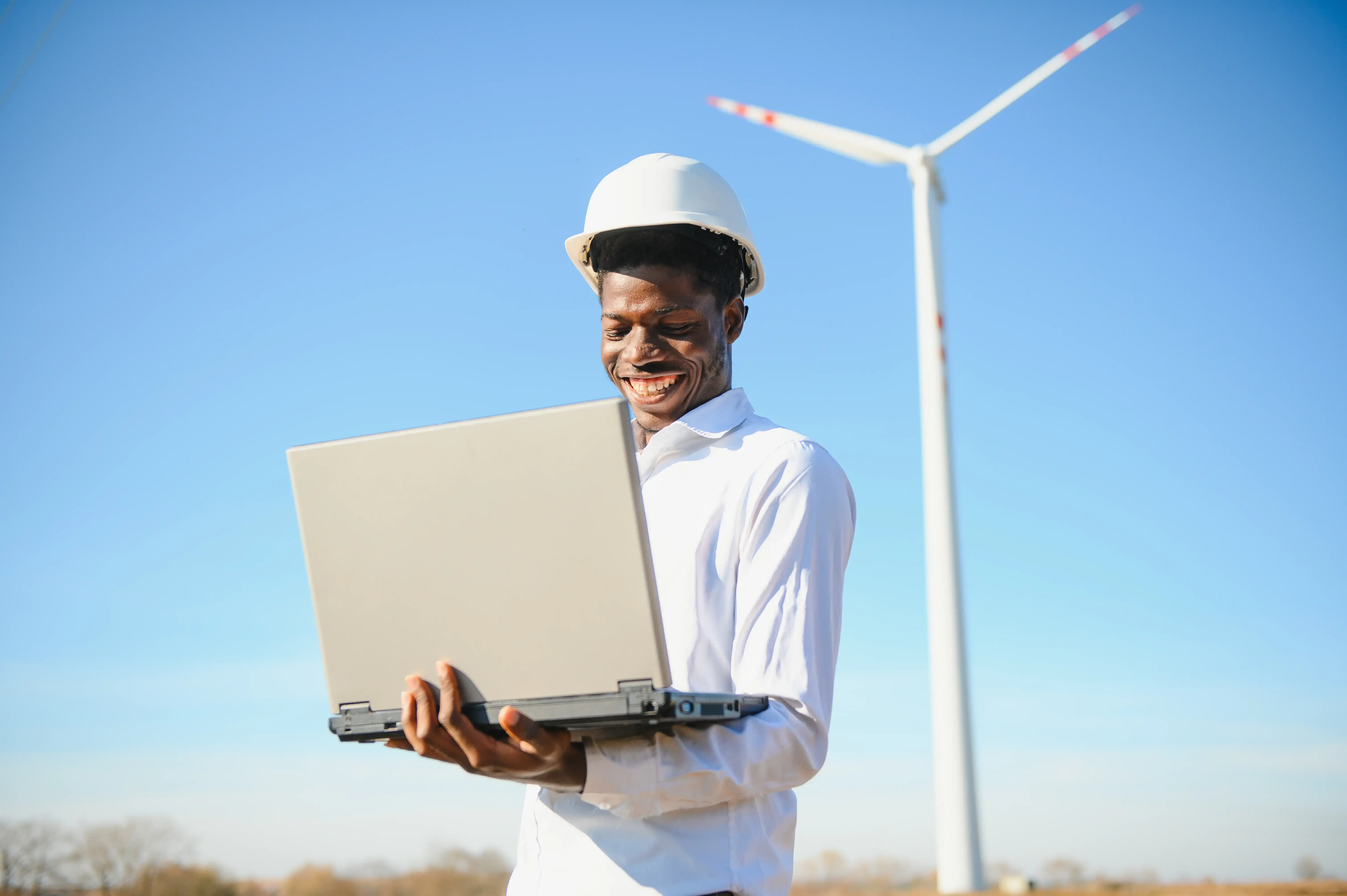 Engineer on laptop outside by a wind combine